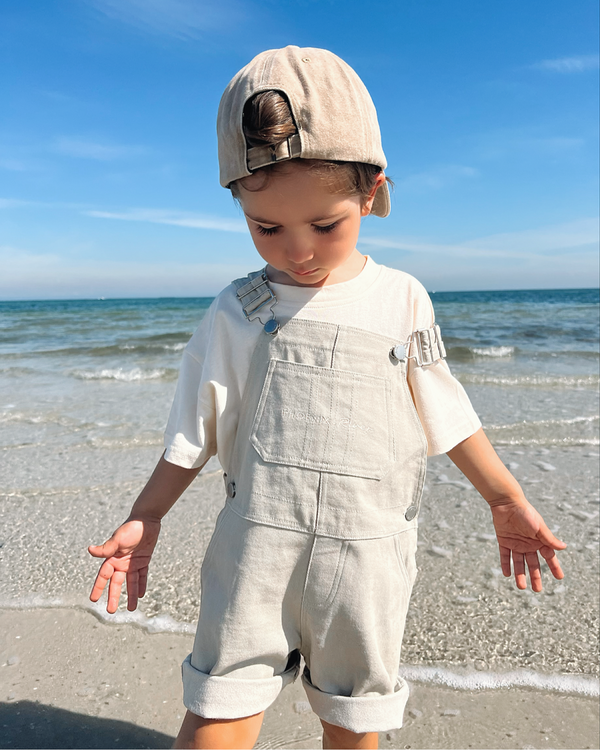Boy wearing white logo tee with beach days overalls at the beach