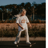 Girl riding a skateboard and wearing the Sun Dance Tee and Flares